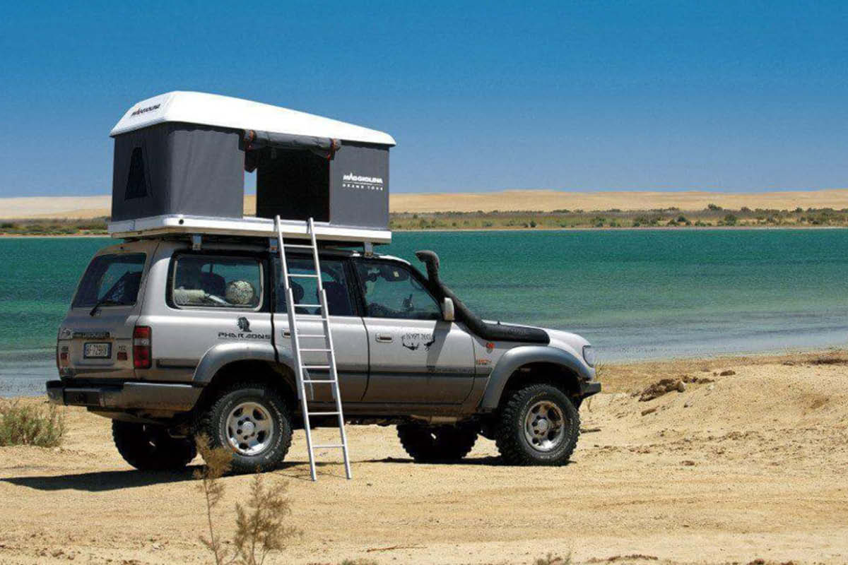Das Bild zeigt einen Grauen Geländewagen mit Dachzelt vor einem See