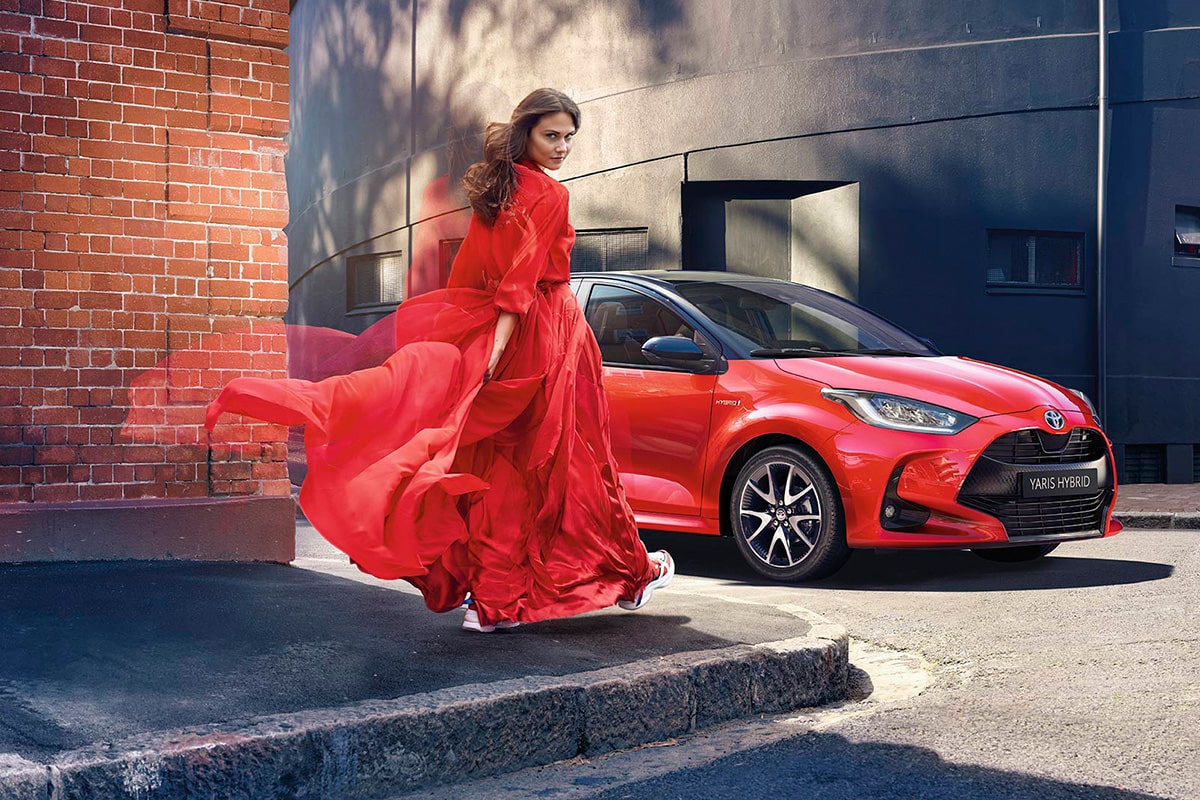 Frau in einem roten Kleid vor einem roten Toyota Yaris